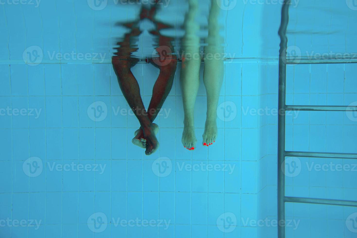 as pernas do homem afro-americano adulto e as pernas da mulher caucasiana debaixo d'água na piscina. conceito de esporte, recreação, férias e amizade foto