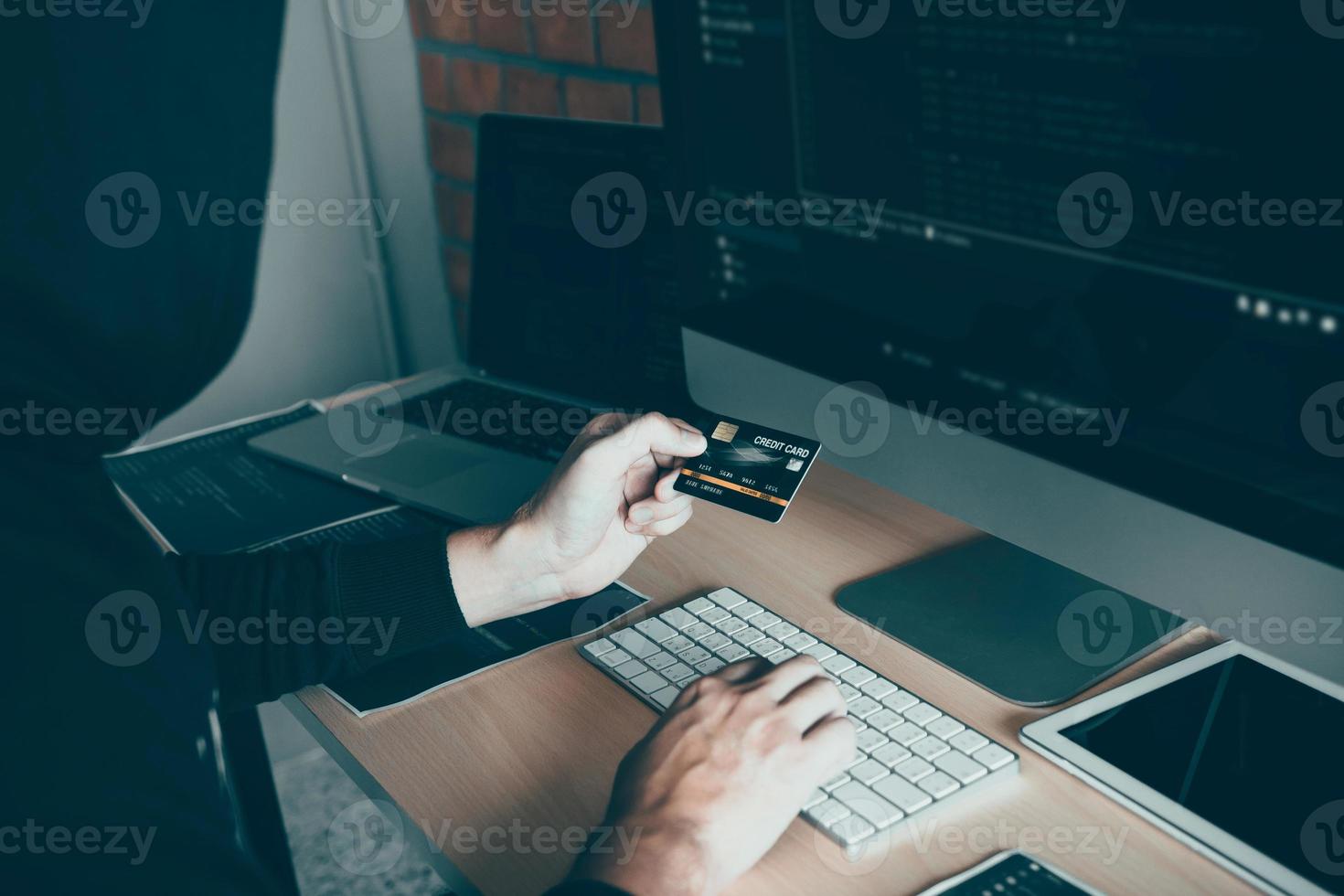 hacker no capô trabalhando com computador e segurando o cartão de crédito com o conceito de hacking de pagamento. foto