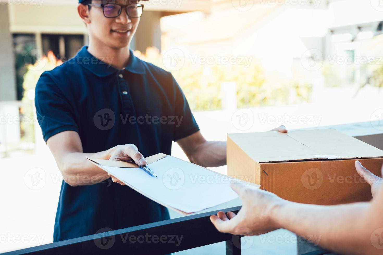jovem asiático sorrindo ao entregar uma caixa de papelão para a mulher segurando o documento para assinar a assinatura. foto