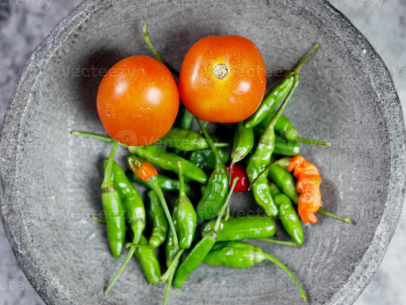 pimenta caiena e tomate em um almofariz de pedra. receita de molho de tomate. conceito de cozimento de alimentos. vista do topo foto