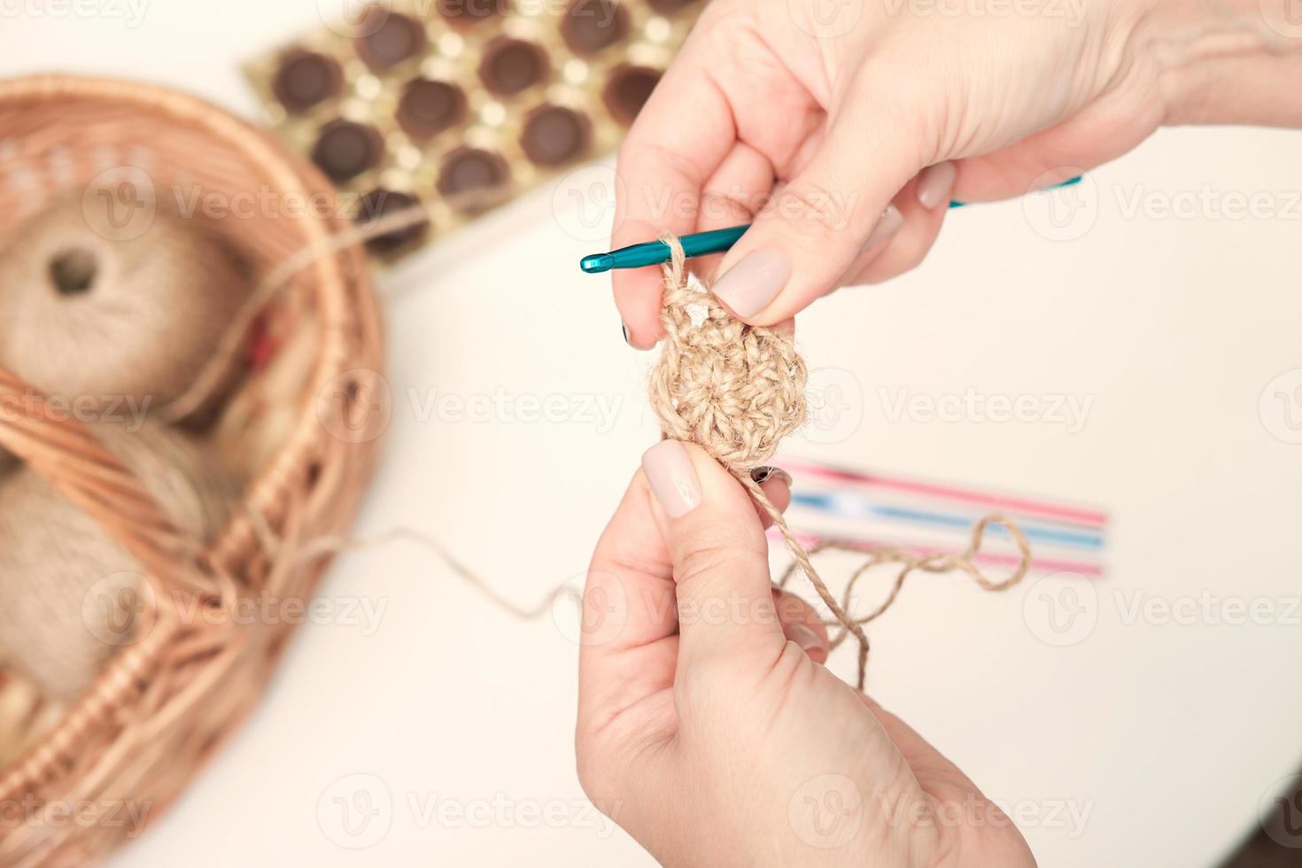 mãos de uma mulher segurando crochê e fio de juta e fragmento de um padrão de malha. tricô ecológico natural, porta copos feita à mão. artesanato e passatempo. decoração ecológica foto