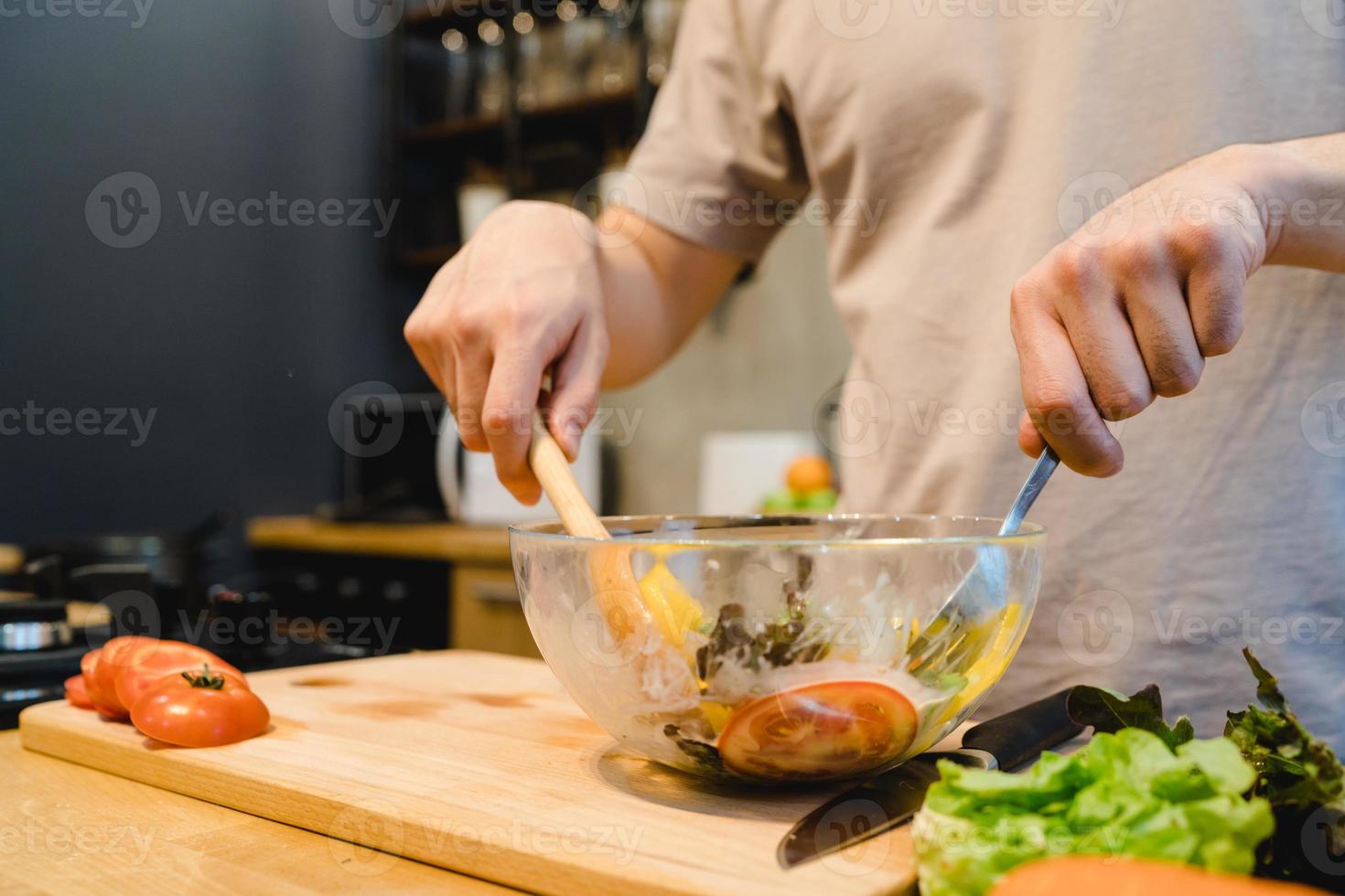 feliz lindo homem asiático preparar comida de salada na cozinha. jovem macho asiático cozinhando comida saudável enquanto fica em casa. estilo de vida do homem em casa conceito. foto