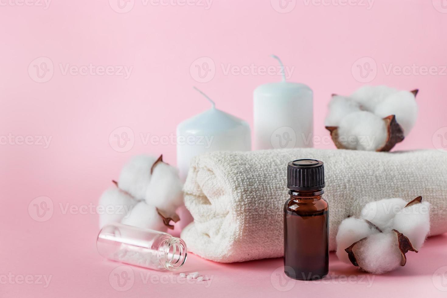 produtos cosméticos naturais para spa e aromaterapia. conceito de relaxamento. velas, flores e uma toalha em um fundo rosa. foto