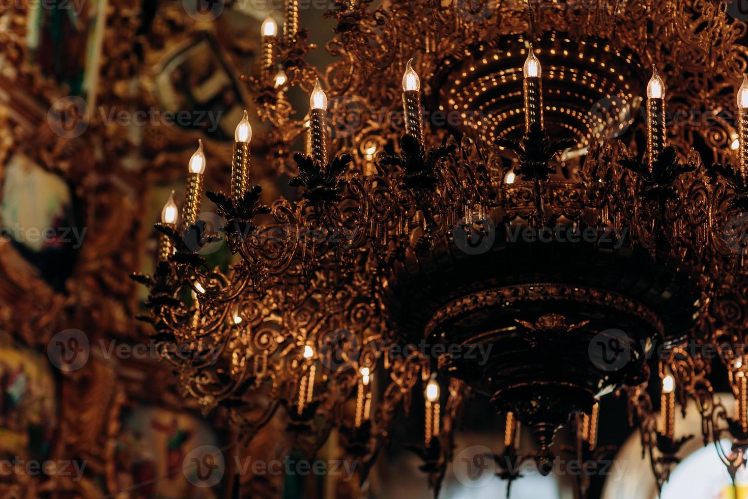 lustre folheado a ouro pendurado na antiga igreja perto dos ícones. lâmpadas modernas são como velas. foto