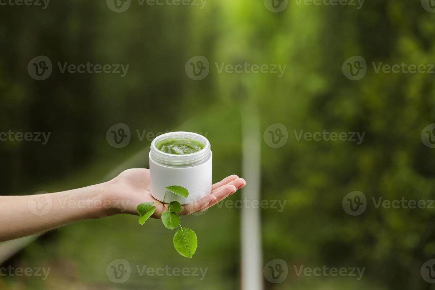 mão feminina jovem segura um pote de creme natural verde para rosto ou corpo. produtos orgânicos naturais para a pele em fundo verde natural. embalagem de loção ou creme. conceito de cuidados com a pele cosméticos de beleza. foto