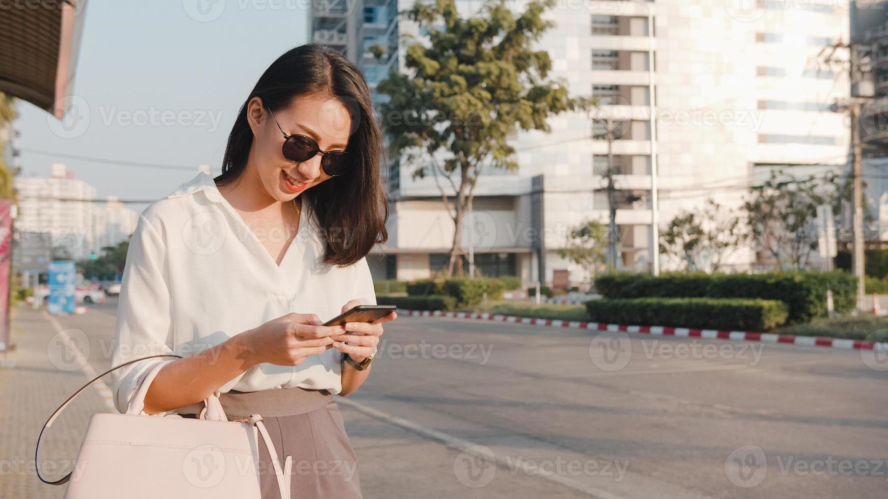 bem sucedida jovem empresária da ásia em roupas de escritório de moda saudando na estrada pegando táxi e segurando o telefone inteligente em pé ao ar livre na cidade moderna urbana. negócio em movimento conceito. foto