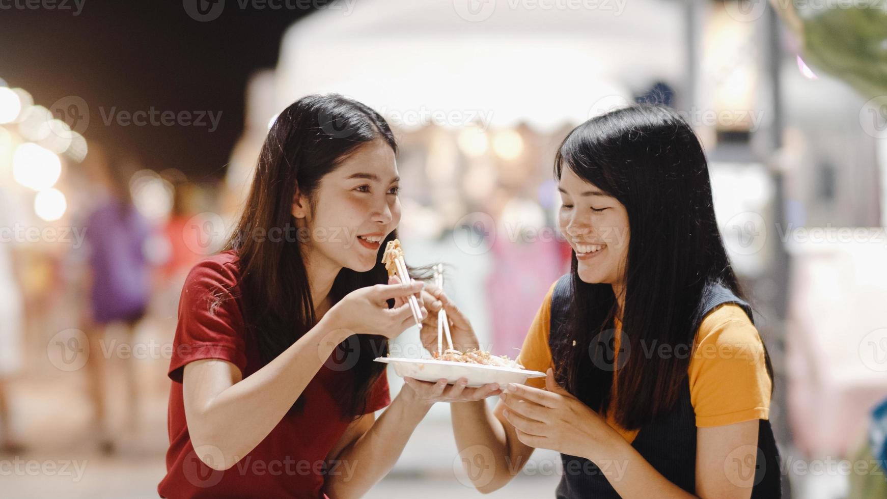 amigos de mulheres jovens asiáticas viajam em bangkok, tailândia, linda fêmea se sentindo feliz andando e comendo pad thai na estrada khao san. as mulheres viajam comem comida de rua no conceito de tailândia. foto