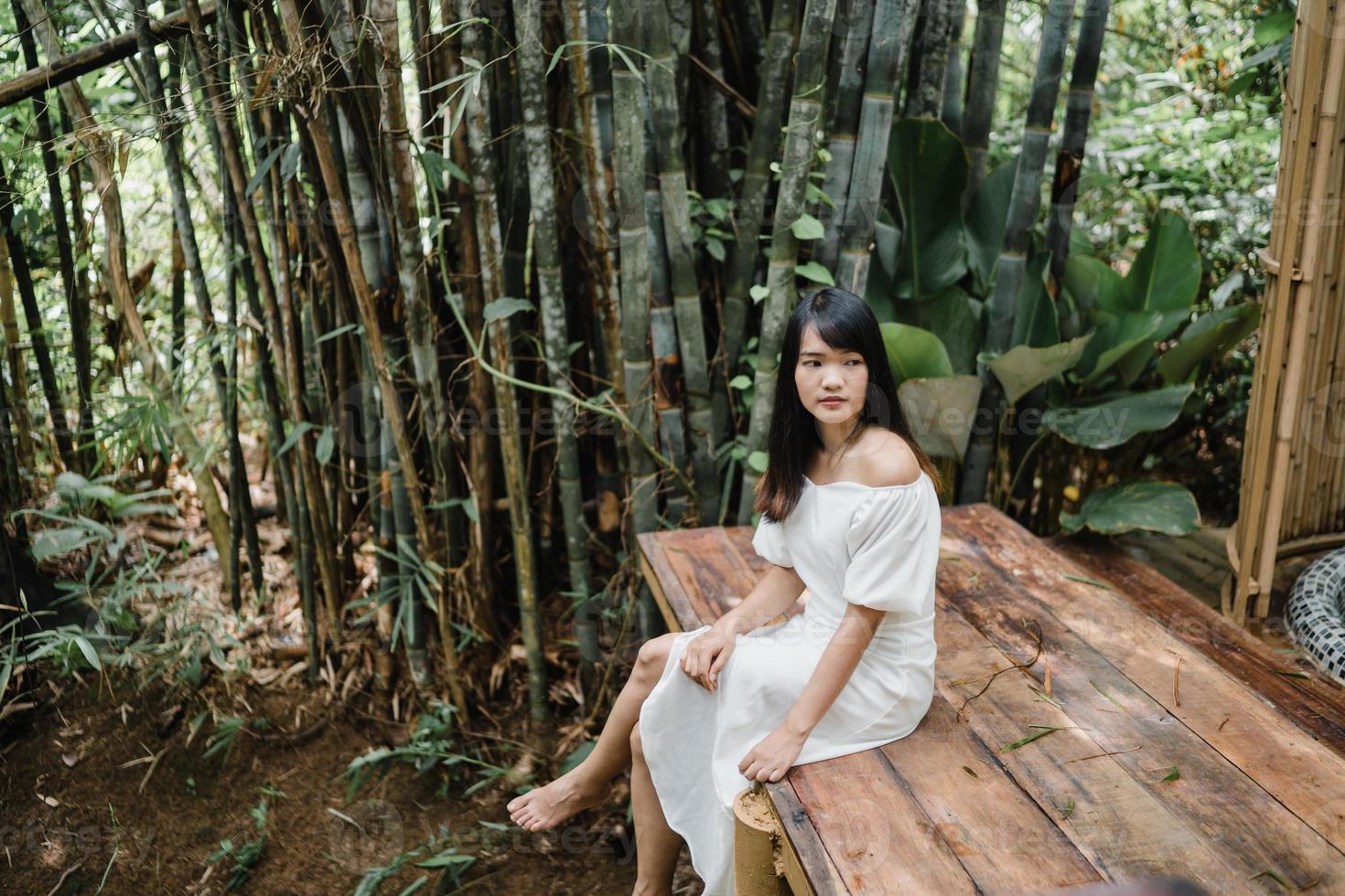 jovem mulher asiática relaxa na floresta, linda fêmea feliz usando o tempo de relaxamento na natureza. mulheres de estilo de vida viajam no conceito de floresta. foto