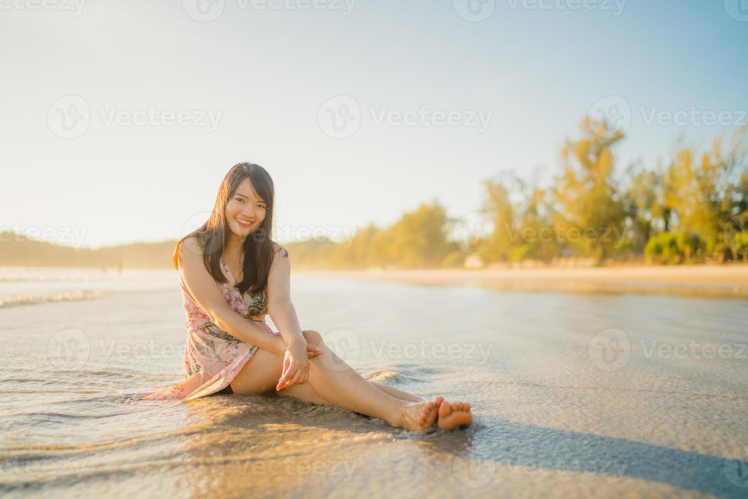 jovem mulher asiática se sentindo feliz na praia, linda fêmea feliz relaxe sorrindo divertido na praia perto do mar ao pôr do sol à noite. mulheres de estilo de vida viajam no conceito de praia. foto