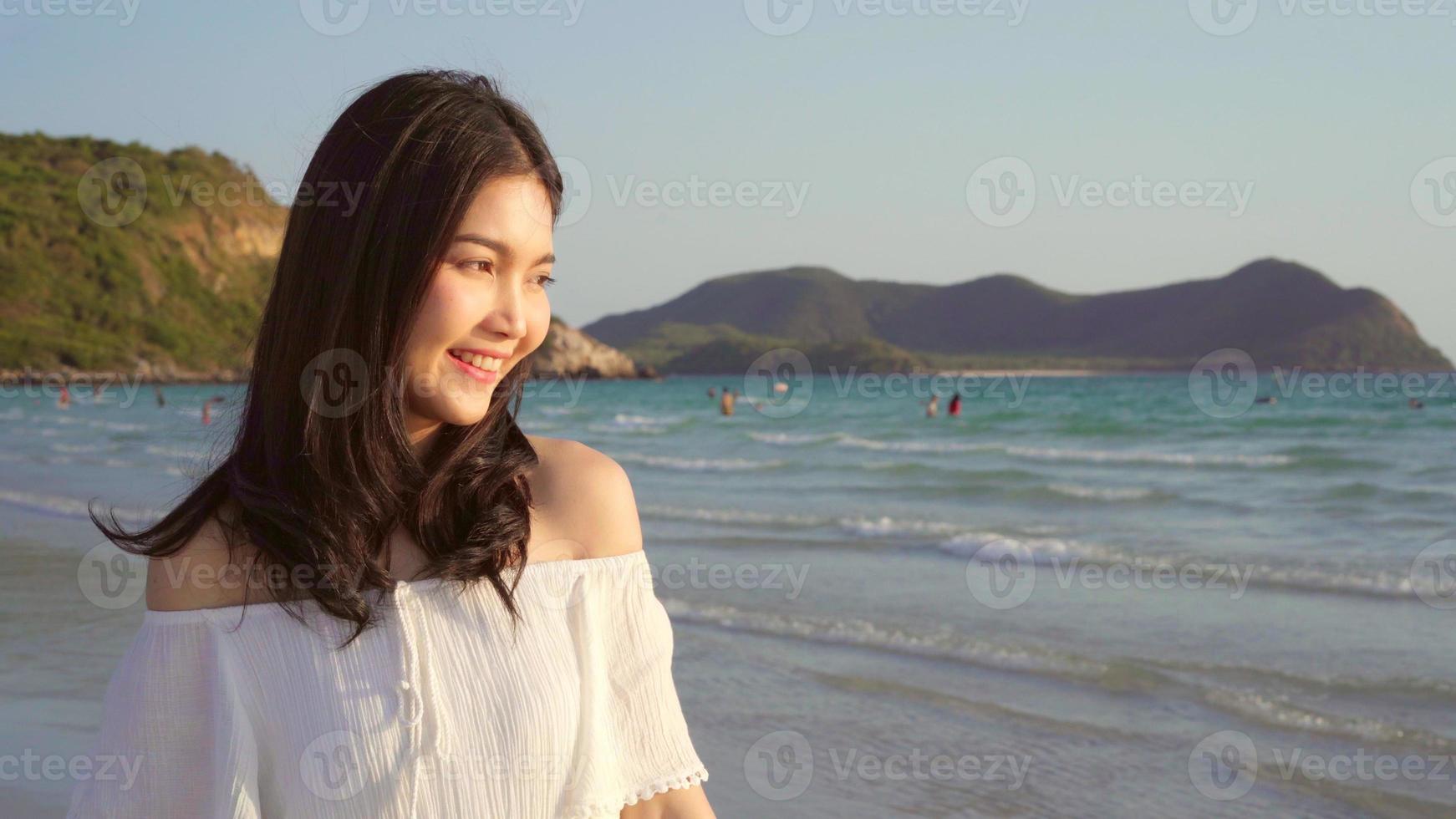 jovem mulher asiática caminhando na praia. linda fêmea feliz relaxe caminhando na praia perto do mar ao pôr do sol à noite. mulheres de estilo de vida viajam no conceito de praia. foto