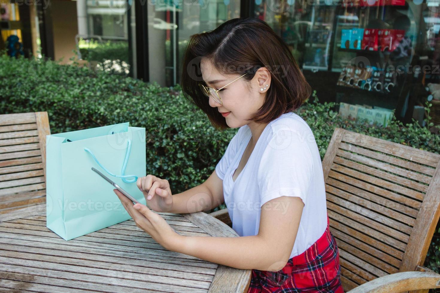 alegre jovem asiática sentada no café usando smartphone para falar, ler e enviar mensagens de texto. mulher asiática atraente olhando em seu telefone. conceito de estilo de vida de mulheres. foto