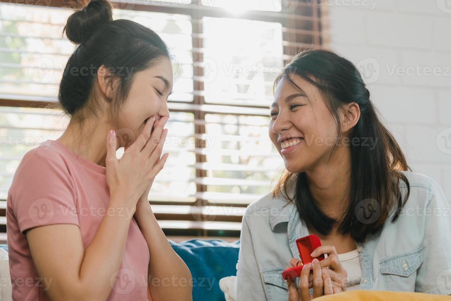 asian lésbicas lgbtq mulheres casal propor em casa, jovem amante da ásia feminino feliz sorrindo ter tempo romântico ao propor e casamento surpresa usar anel de casamento na sala de estar em casa conceito. foto