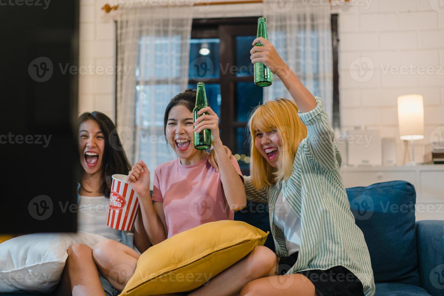 grupo de mulheres asiáticas festa em casa, feminino bebendo cerveja assistindo tv cheer futebol momento engraçado juntos no sofá na sala de estar à noite. fã de futebol adolescente jovem amigo, comemore o conceito de férias. foto