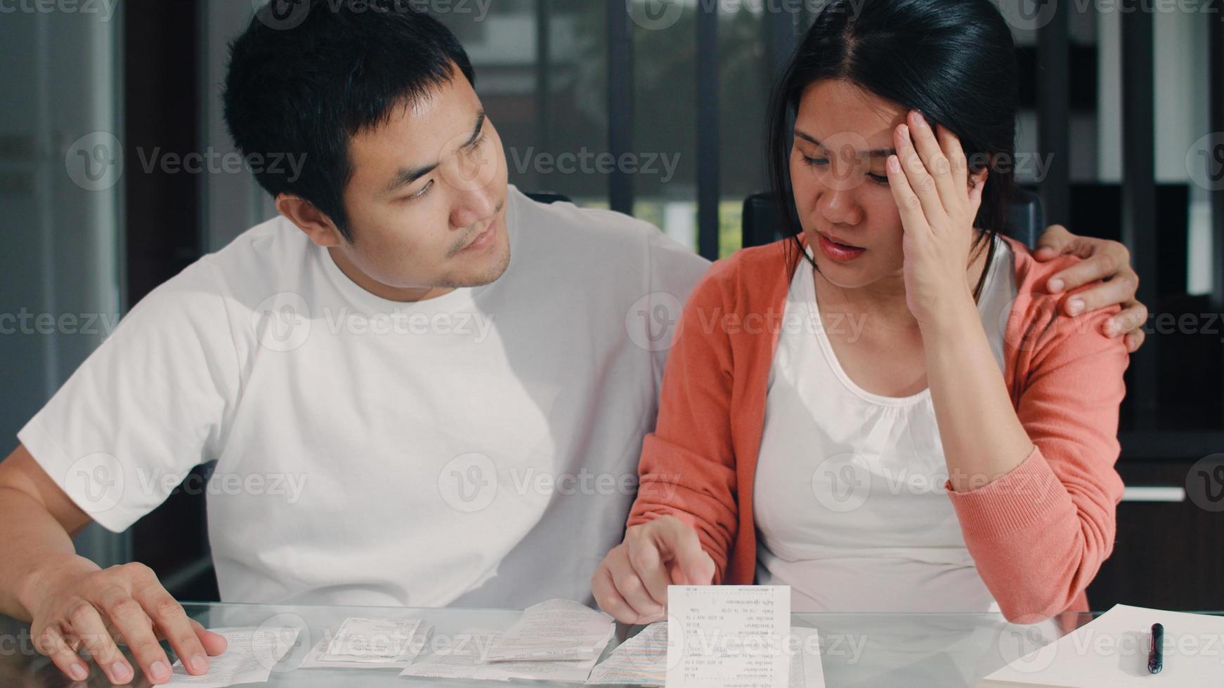 jovem casal asiático grávida registros de receitas e despesas em casa. mãe preocupada, séria, estressada enquanto registra orçamento, imposto, documento financeiro trabalhando no conceito de sala de estar em casa. foto