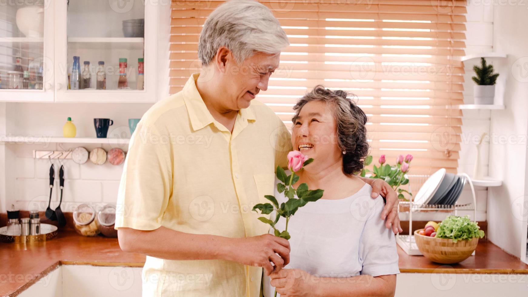 casal de idosos asiáticos se sentindo feliz sorrindo e segurando flores e olhando para a câmera enquanto relaxa na cozinha em casa. família sênior de estilo de vida aproveite o conceito de tempo em casa. retrato olhando para a câmera. foto