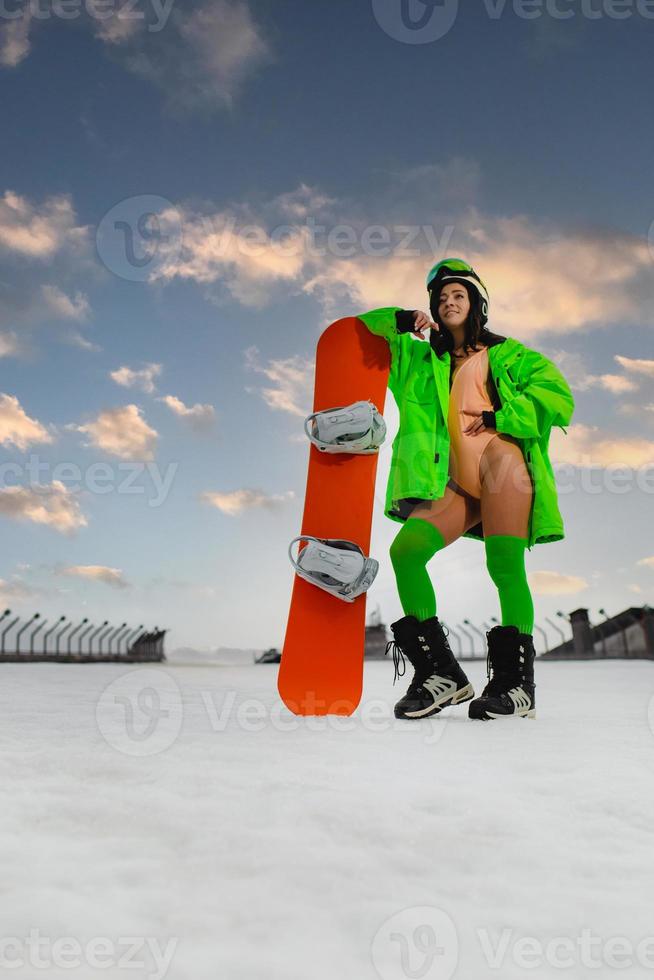 jovem mulher bonita posando com uma prancha de snowboard em uma pista de esqui foto