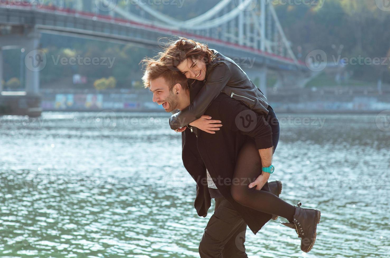 lindo incrível engraçado alegre jovem casal abraçando ao ar livre à beira do rio no fundo da ponte. namorada e namorado. conceito de família, amor e amizade foto