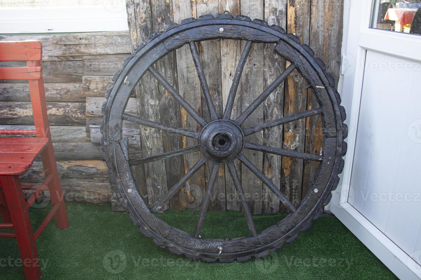 roda de carroça de madeira velha esquecida encostada a uma parede de madeira. estrelinhas na velha parede de madeira da casa. foto