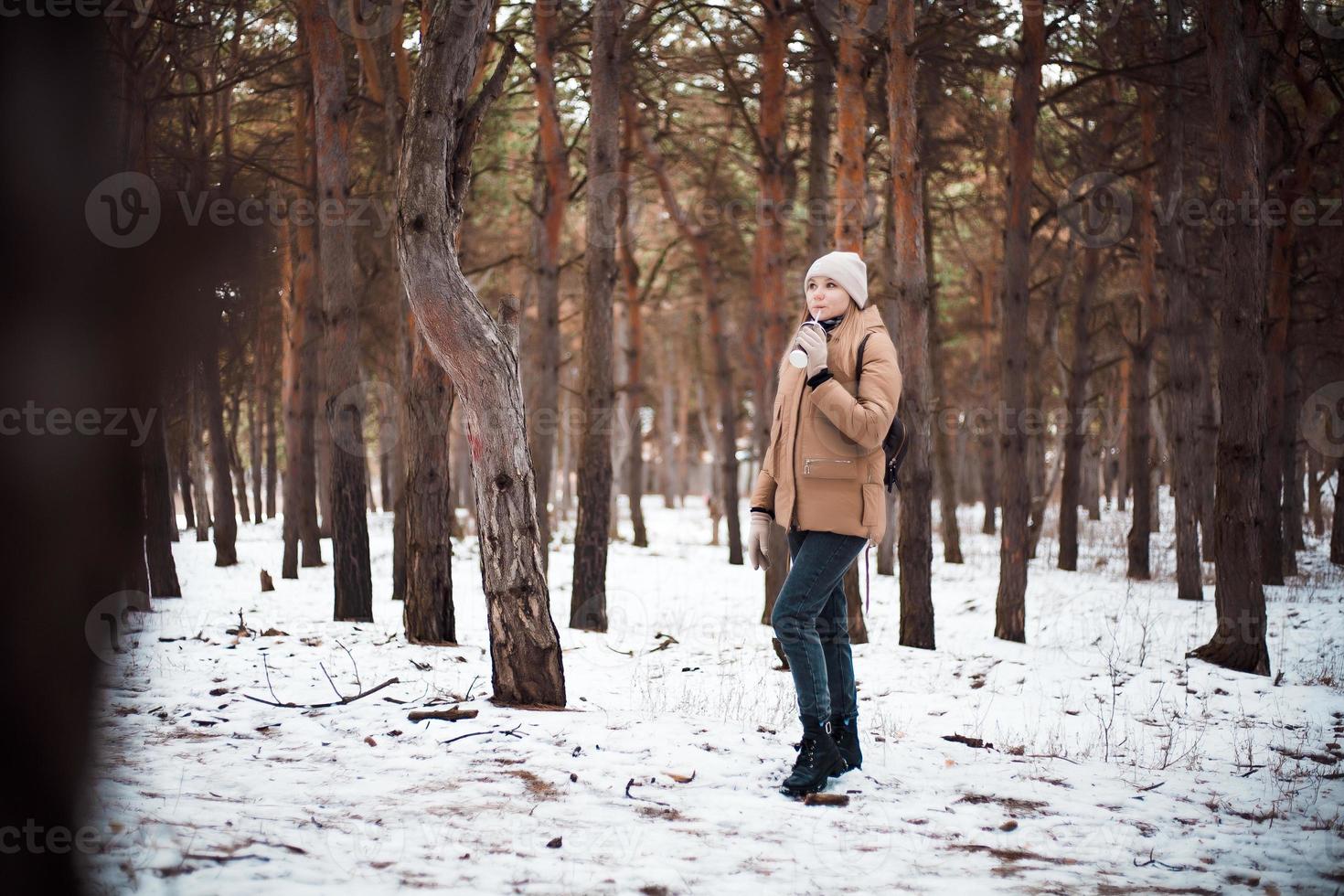 uma jovem com roupas de inverno e uma xícara de bebida quente caminha na floresta de inverno. foto