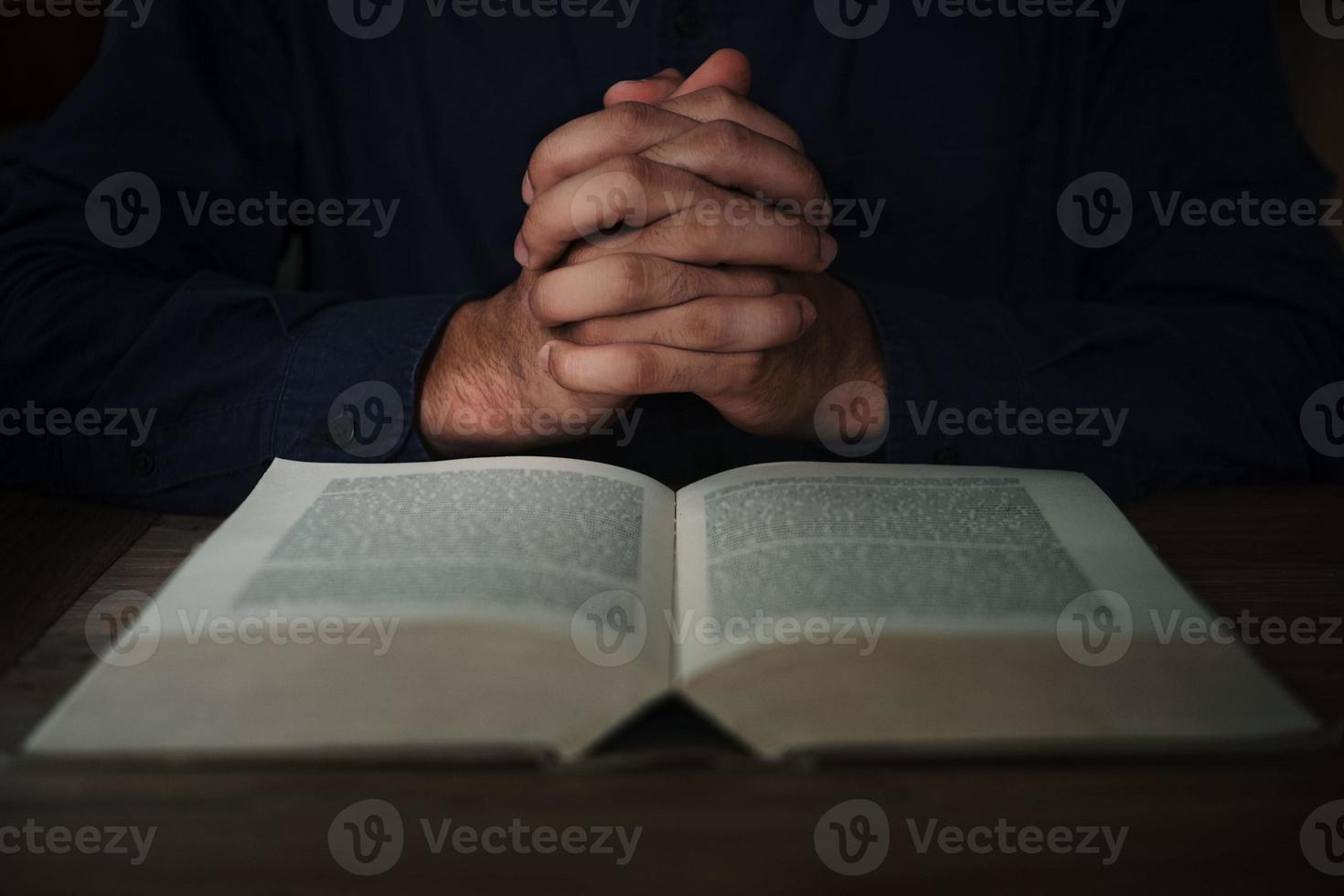 homem está lendo e orando a escritura ou a bíblia sagrada em uma mesa de madeira com espaço de cópia. religião, acredite no conceito. foto