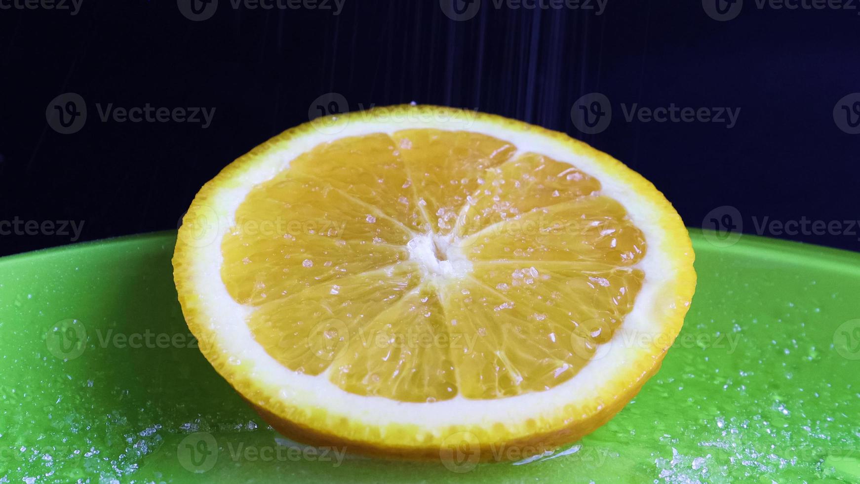 uma fatia redonda de laranja que parece muito suculenta e apetitosa polvilhada com açúcar. close-up de açúcar em uma fatia recém-cortada de frutas cítricas em um prato verde, em um fundo preto foto