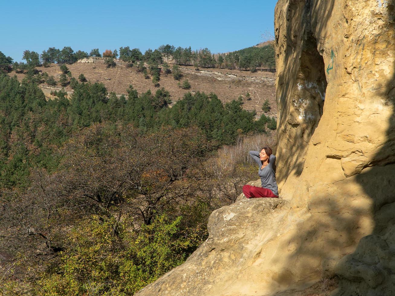 mulher com olhos fechados e braços atrás da cabeça, sentado em uma montanha na posição de lótus em meditação em um dia de outono foto