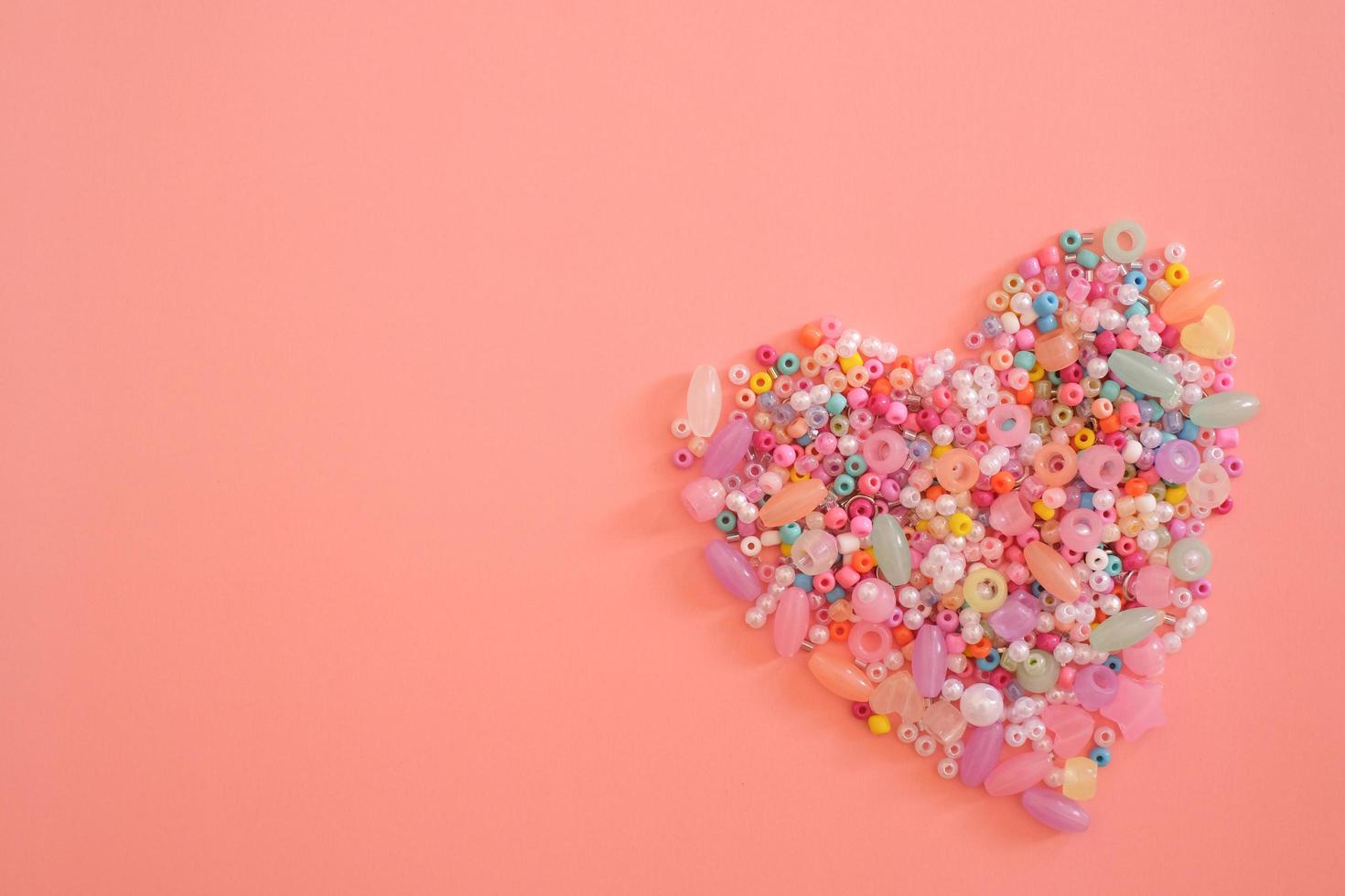 forma de coração colorido feito de miçangas como um símbolo de amor isolado em fundo rosa claro pastel com espaço de cópia. dia dos namorados, presente, mensagem de amante, cartão de felicitações. conceito de amor. foto