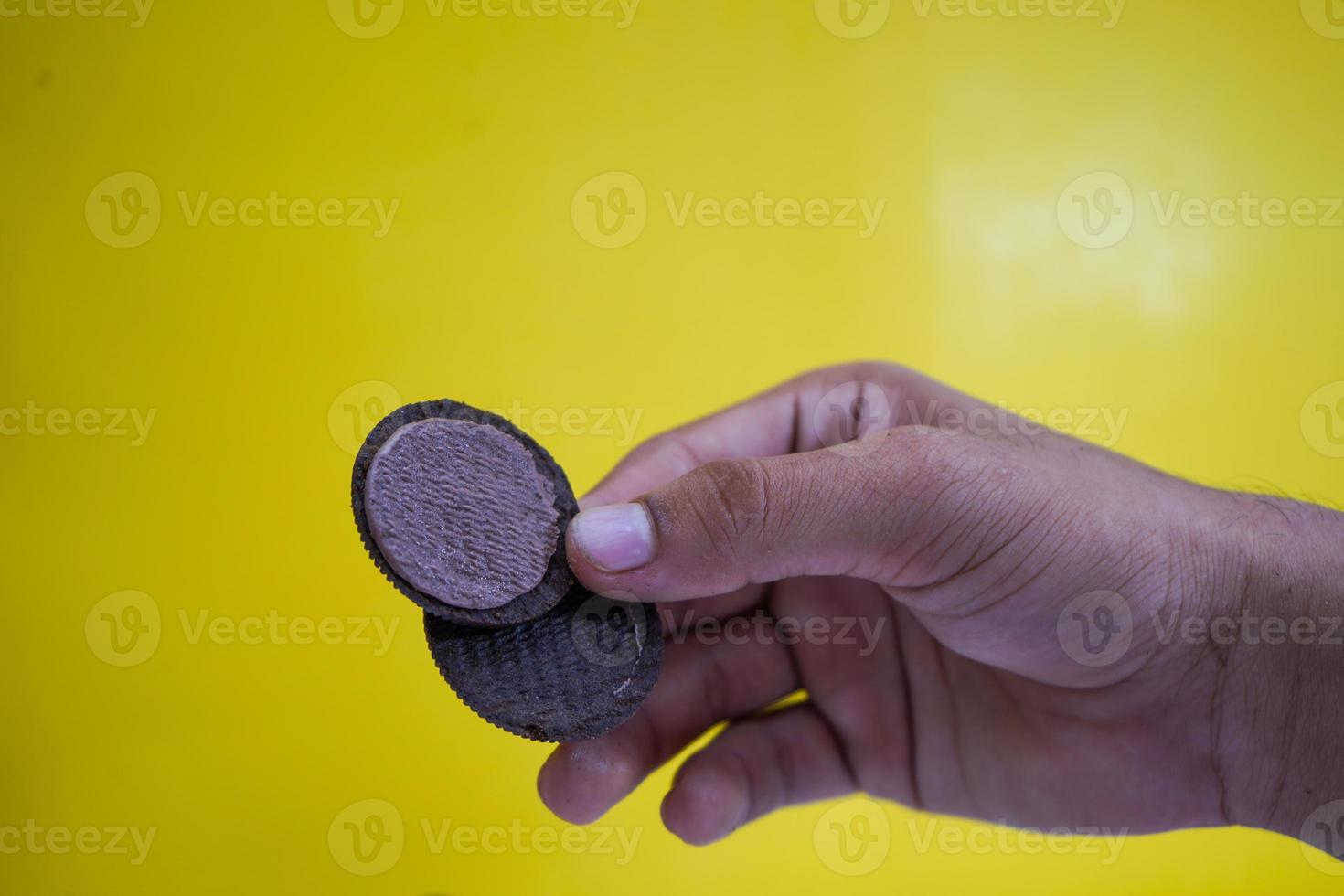 mãos segurando biscoitos de chocolate em um fundo amarelo com espaço de cópia foto
