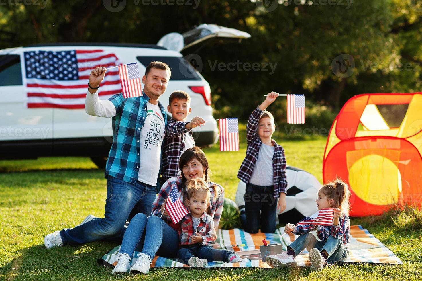 grande família americana passando tempo juntos. com bandeiras dos eua contra grande carro suv ao ar livre. feriado americano. quatro filhos. foto