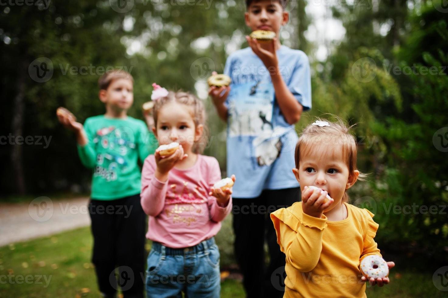 quatro crianças com donuts no quintal à noite. saborosa comida de donut gostoso. foto