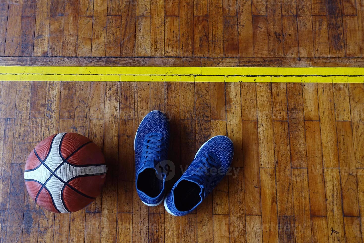 vista superior de sapatos e bola de basquete na quadra de basquete de madeira foto