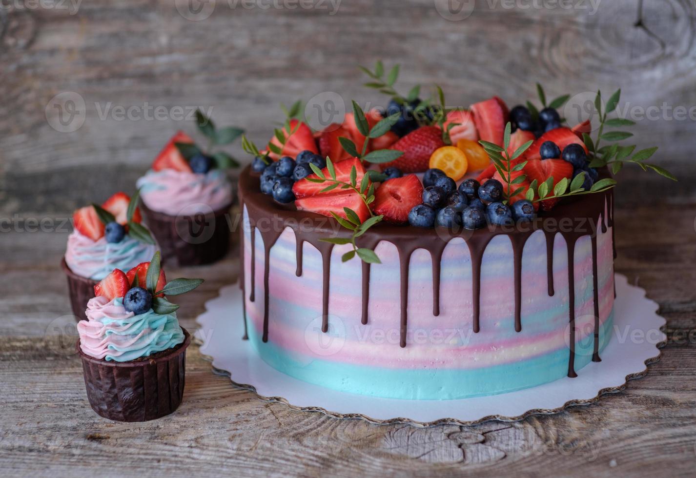 cupcakes caseiros com creme rosa e turquesa, decorados com morangos e mirtilos foto