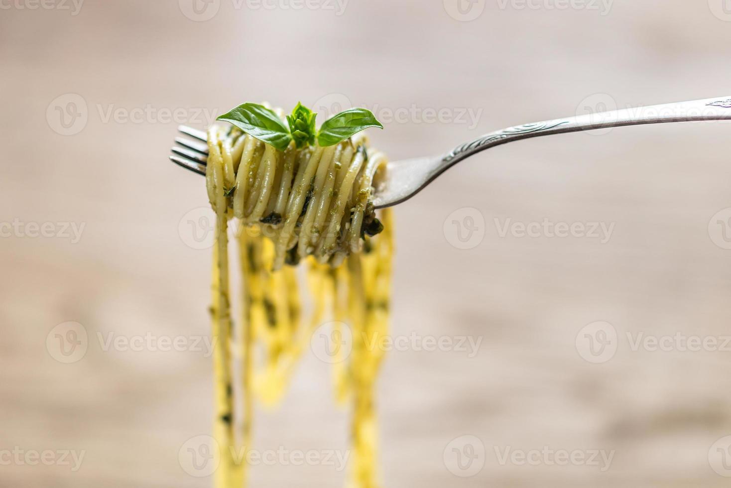 espaguete com molho pesto e folha de manjericão no garfo foto