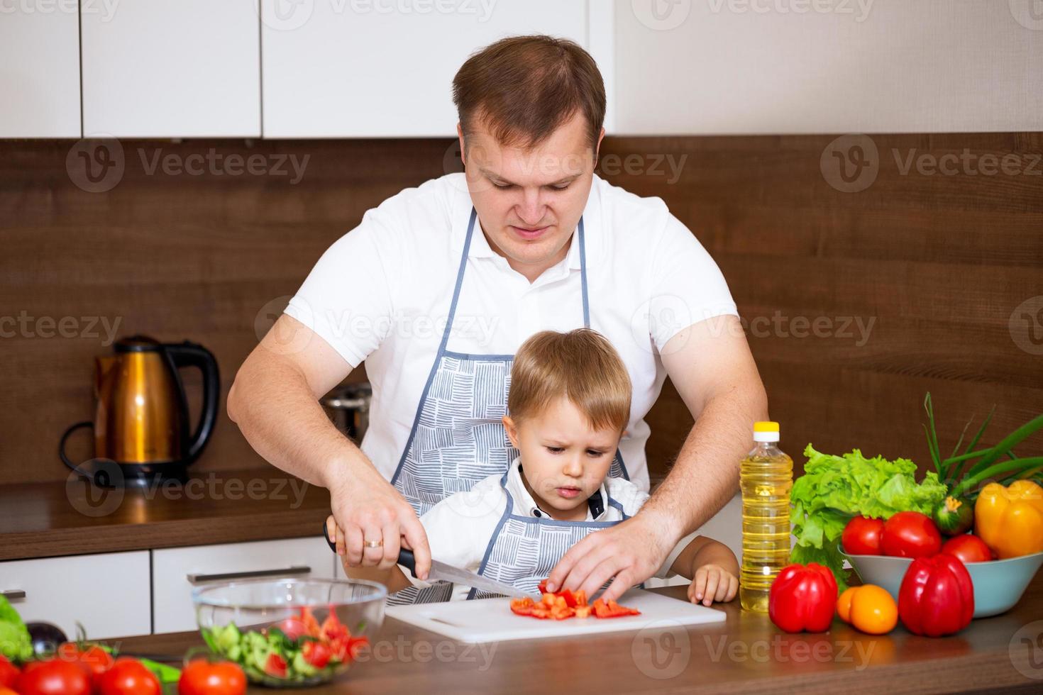 feliz pai ensina filho a cortar salada na cozinha foto