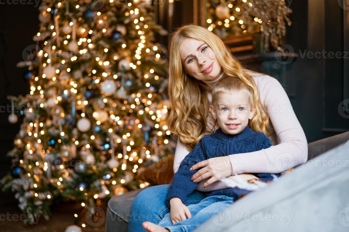 feliz mãe e filho no sofá contra o fundo da árvore de natal decorada foto