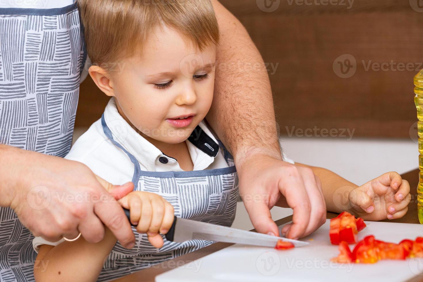 feliz pai ensina filho a cortar salada na cozinha foto