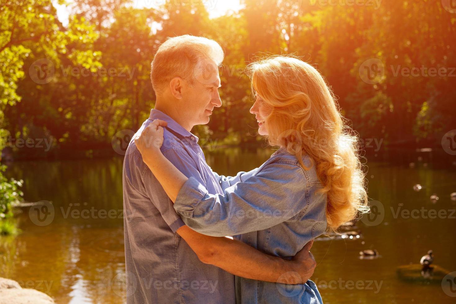 um casal adulto fica na margem do lago em um abraço nos raios do sol poente foto