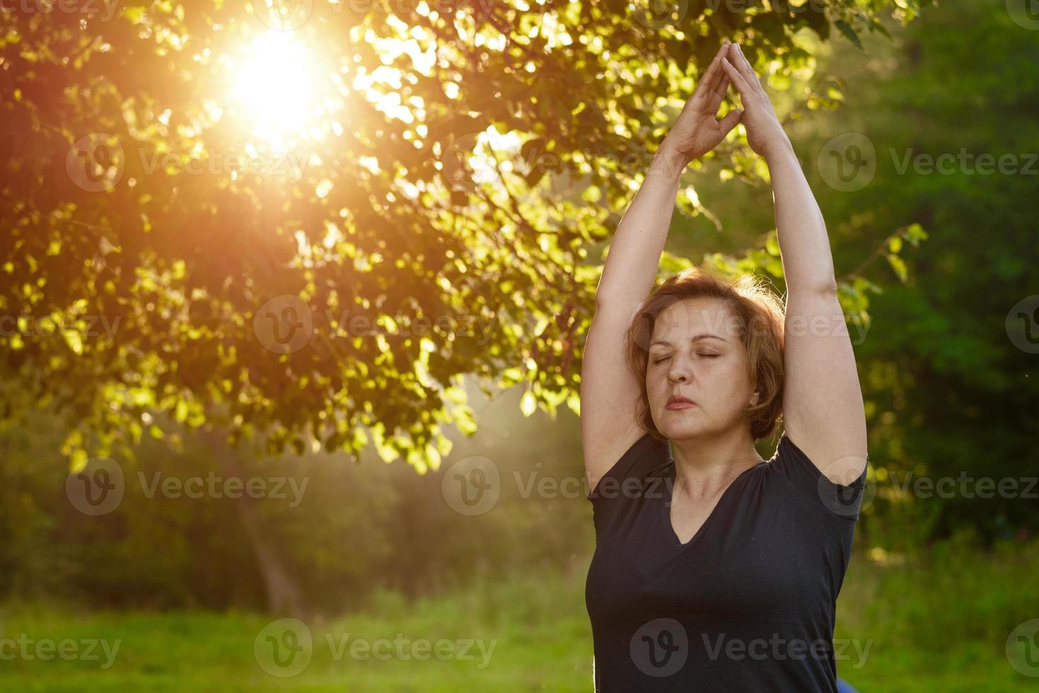 mulher adulta medita com as palmas das mãos dobradas no parque com os olhos fechados foto