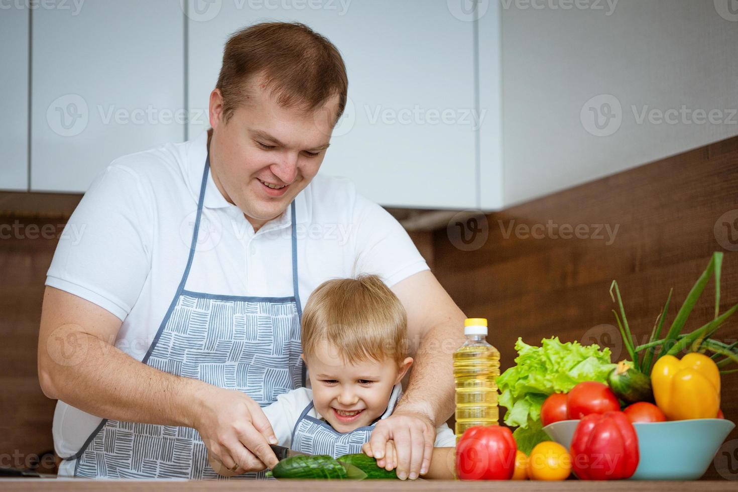 pai e filho preparando uma salada na cozinha, o conceito de cozinhar em família foto