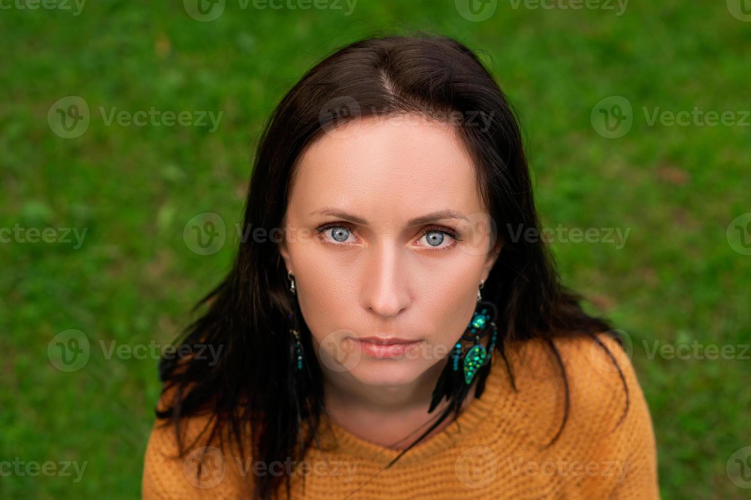 retrato de close-up de uma mulher com cabelos escuros e olhos azuis contra um fundo de grama verde foto