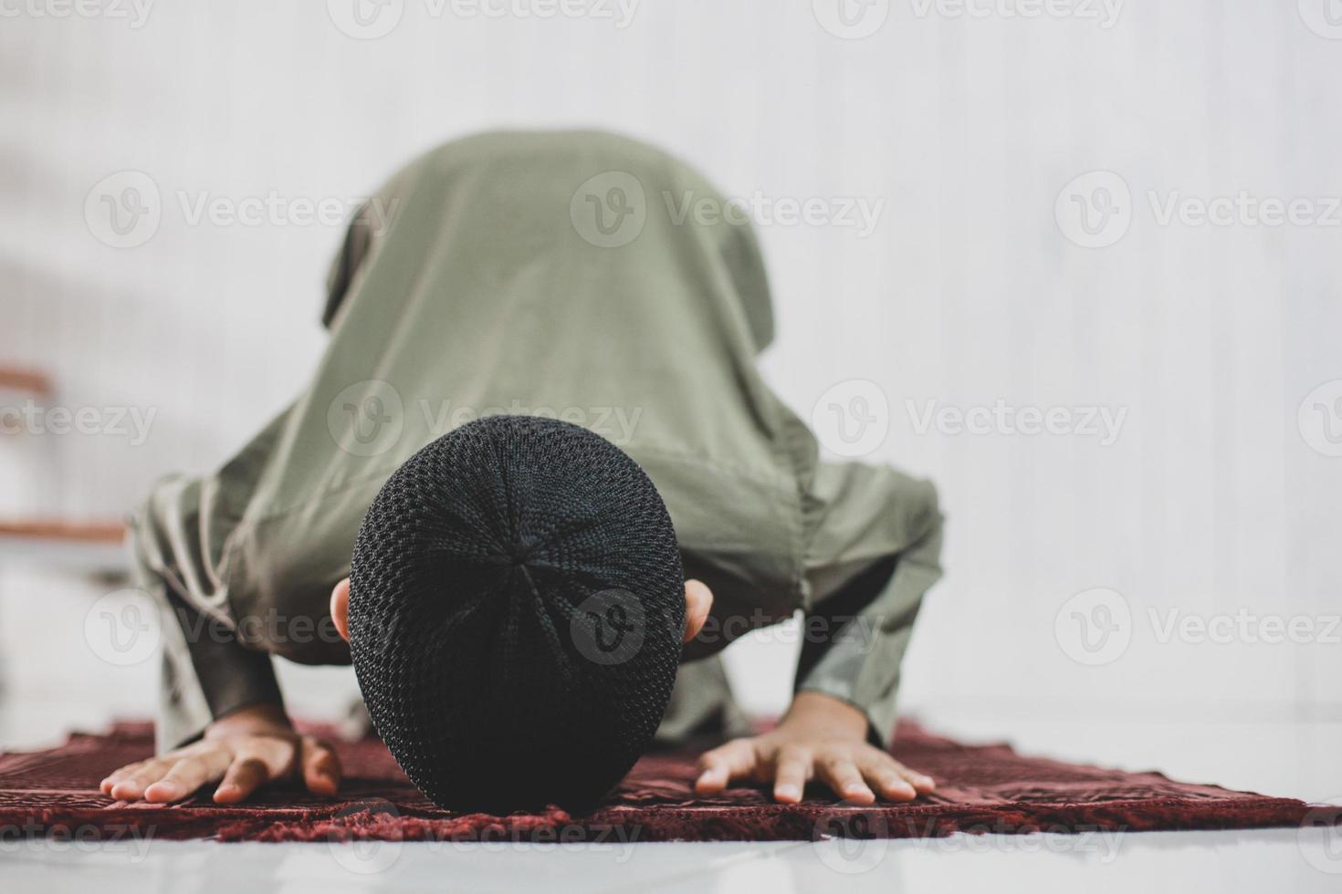 menino muçulmano asiático fazendo salat com pose de prostração no tapete de oração foto