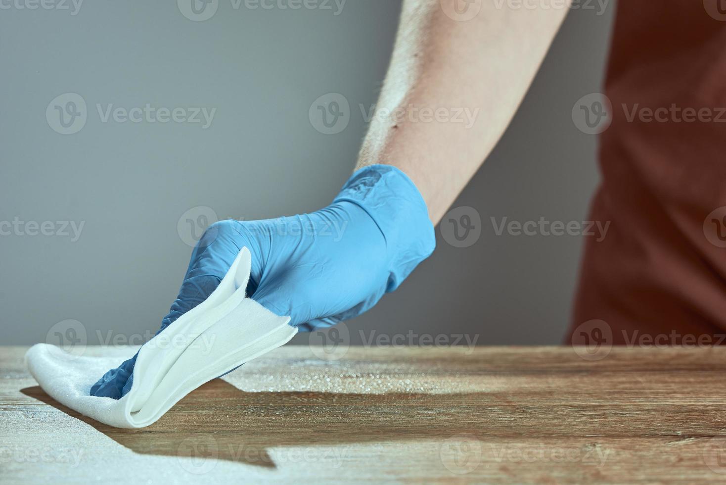 a mão de um homem na luva médica limpa a mesa com guardanapo. garçom de fundo em um avental em desfoque. tratamento da superfície. foto