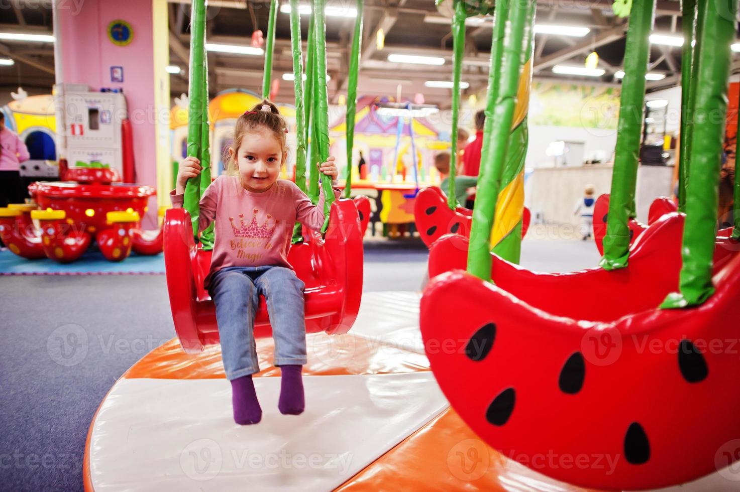 linda menina balançando em balanços no centro de recreação indoor. foto