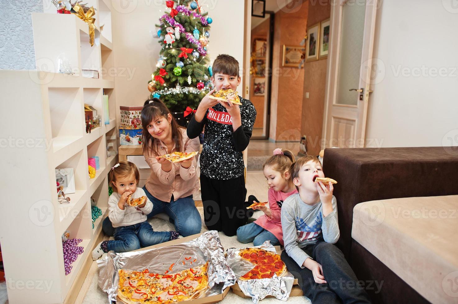 família feliz com quatro filhos comendo pizza em casa. foto