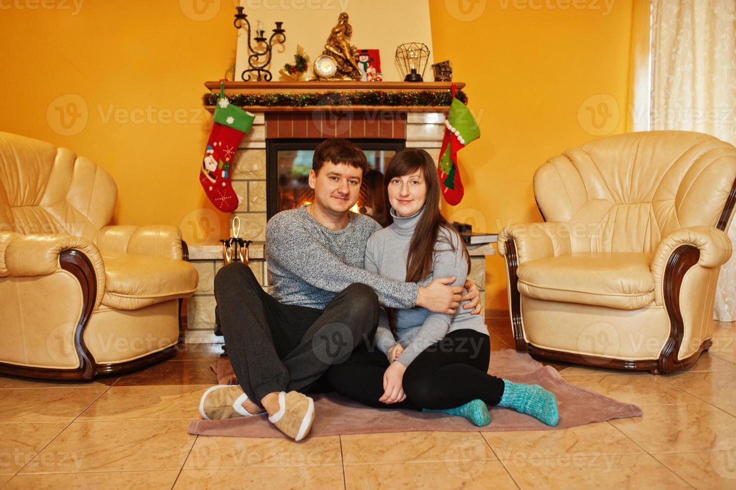 casal jovem feliz em casa por uma lareira na sala de estar quente em dia de inverno. foto