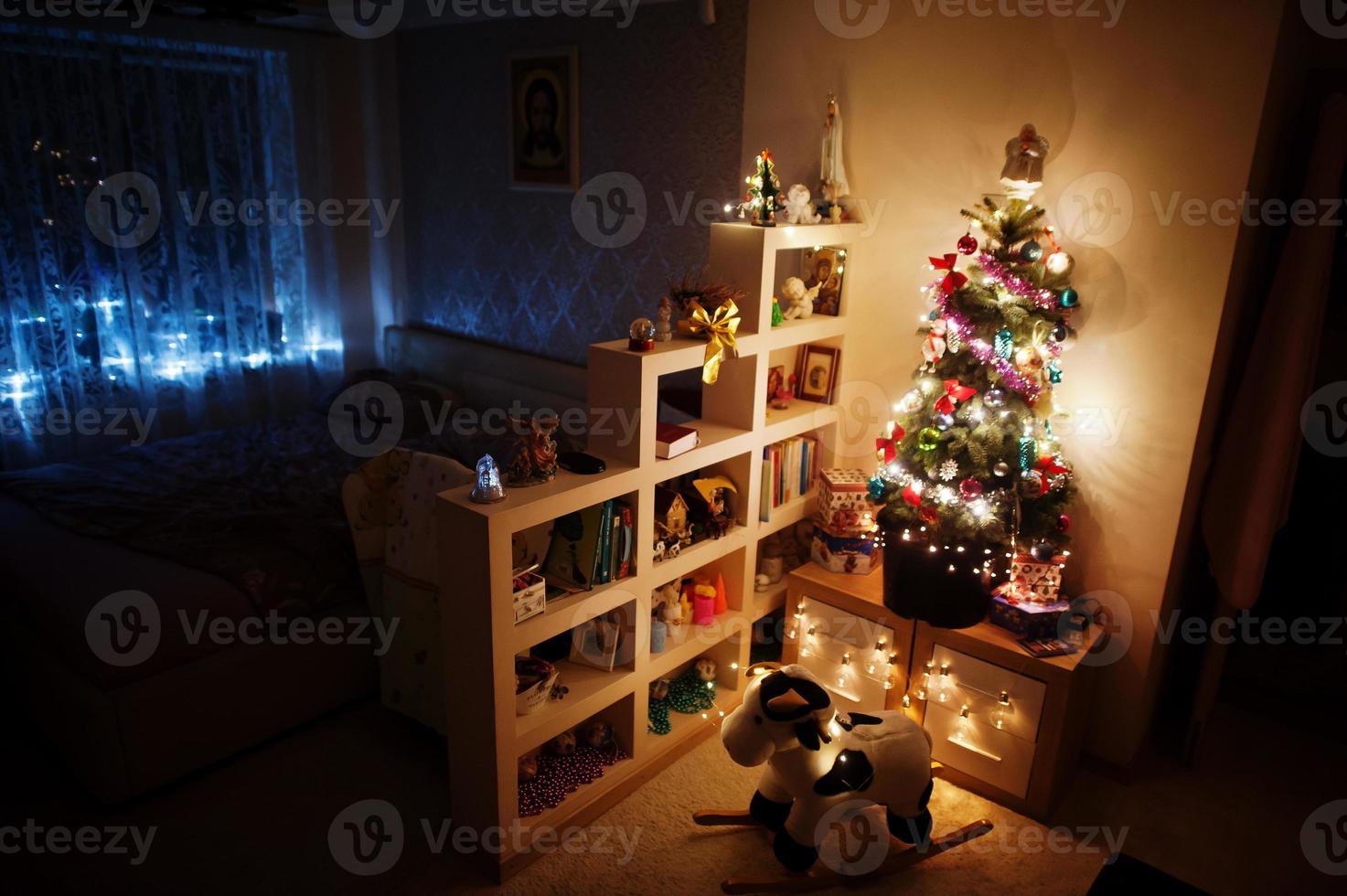 brinquedo de vaca hobby contra árvore de natal com guirlandas brilhantes na noite em casa. foto