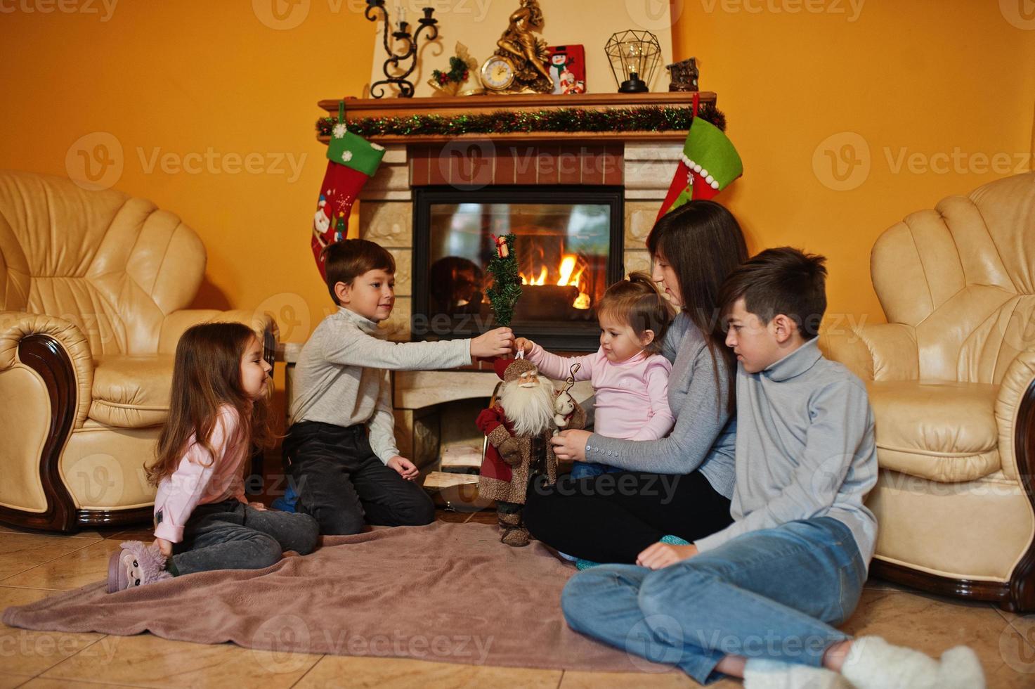 feliz jovem grande família por uma lareira na sala de estar quente em dia de inverno. mãe com quatro filhos em casa. foto