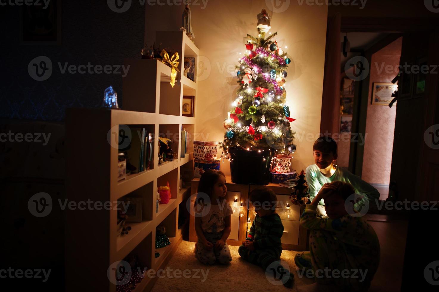 crianças olhando na árvore de natal com guirlandas brilhantes na noite em casa. foto