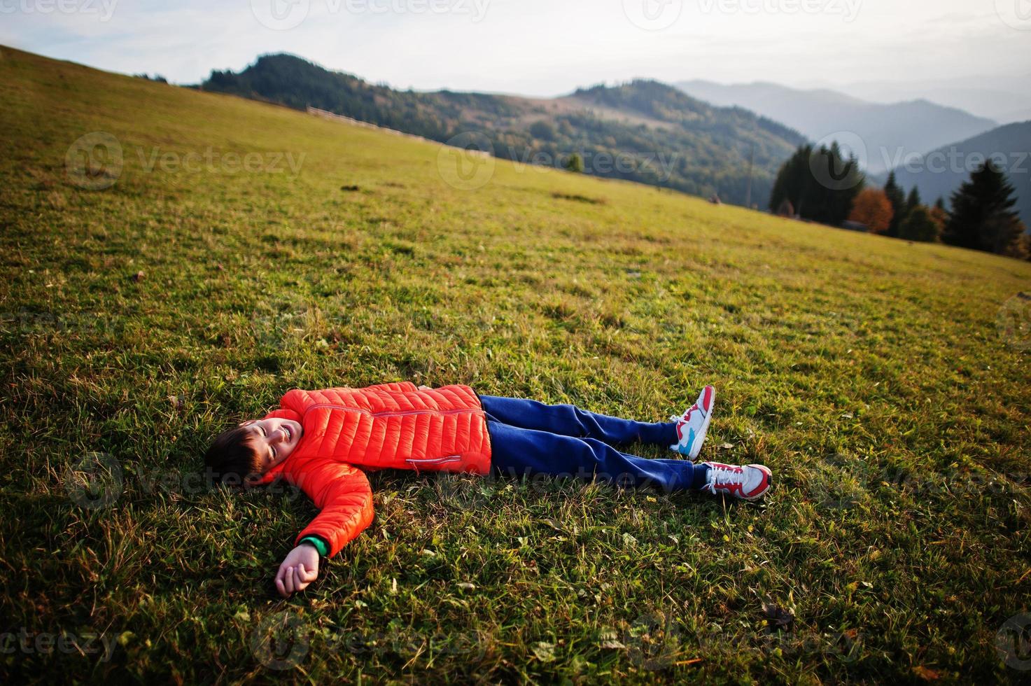 menino deitado na grama com uma linda cordilheira no horizonte. foto