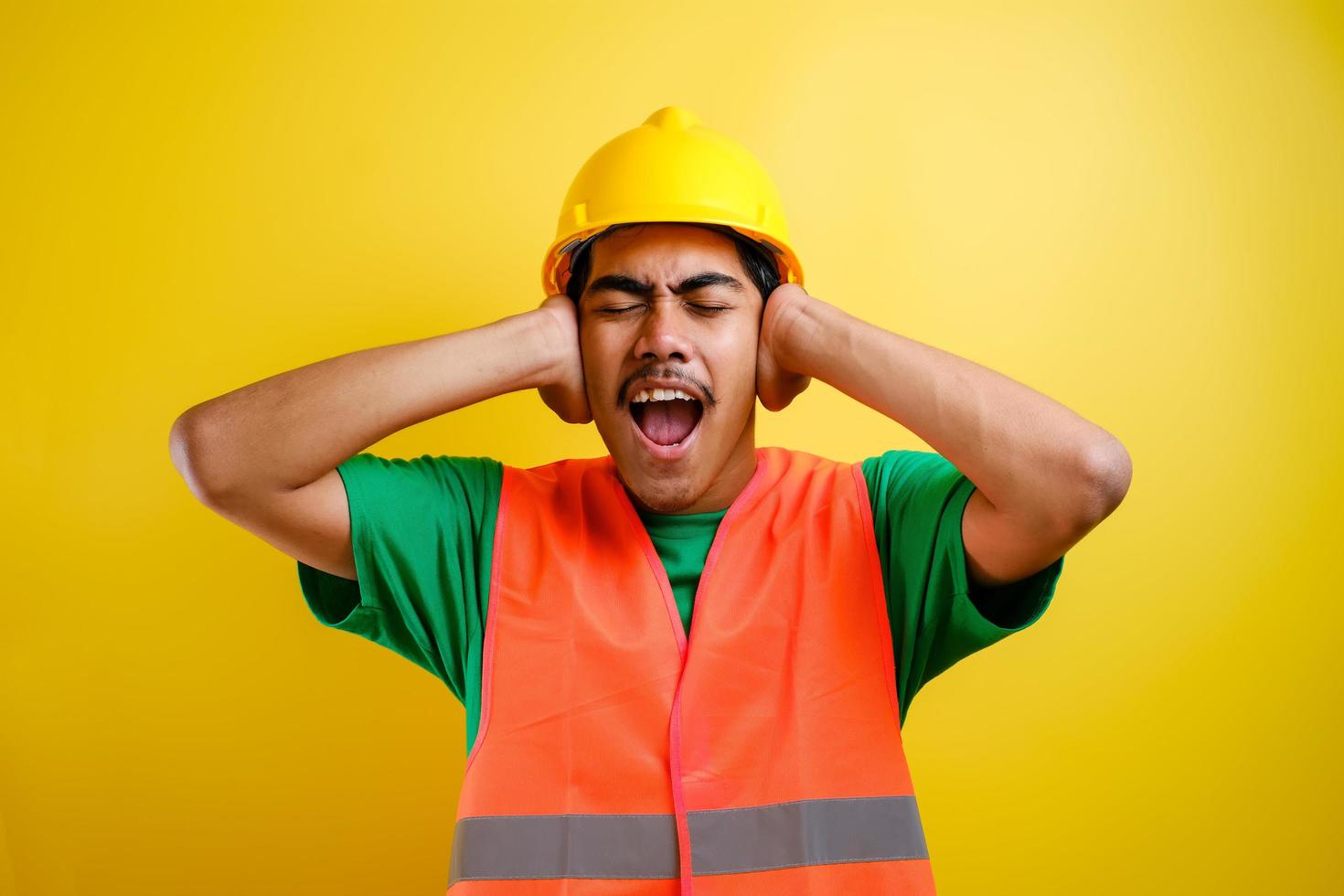 trabalhador usando capacete de segurança cobrindo os ouvidos com os dedos com expressão irritada foto